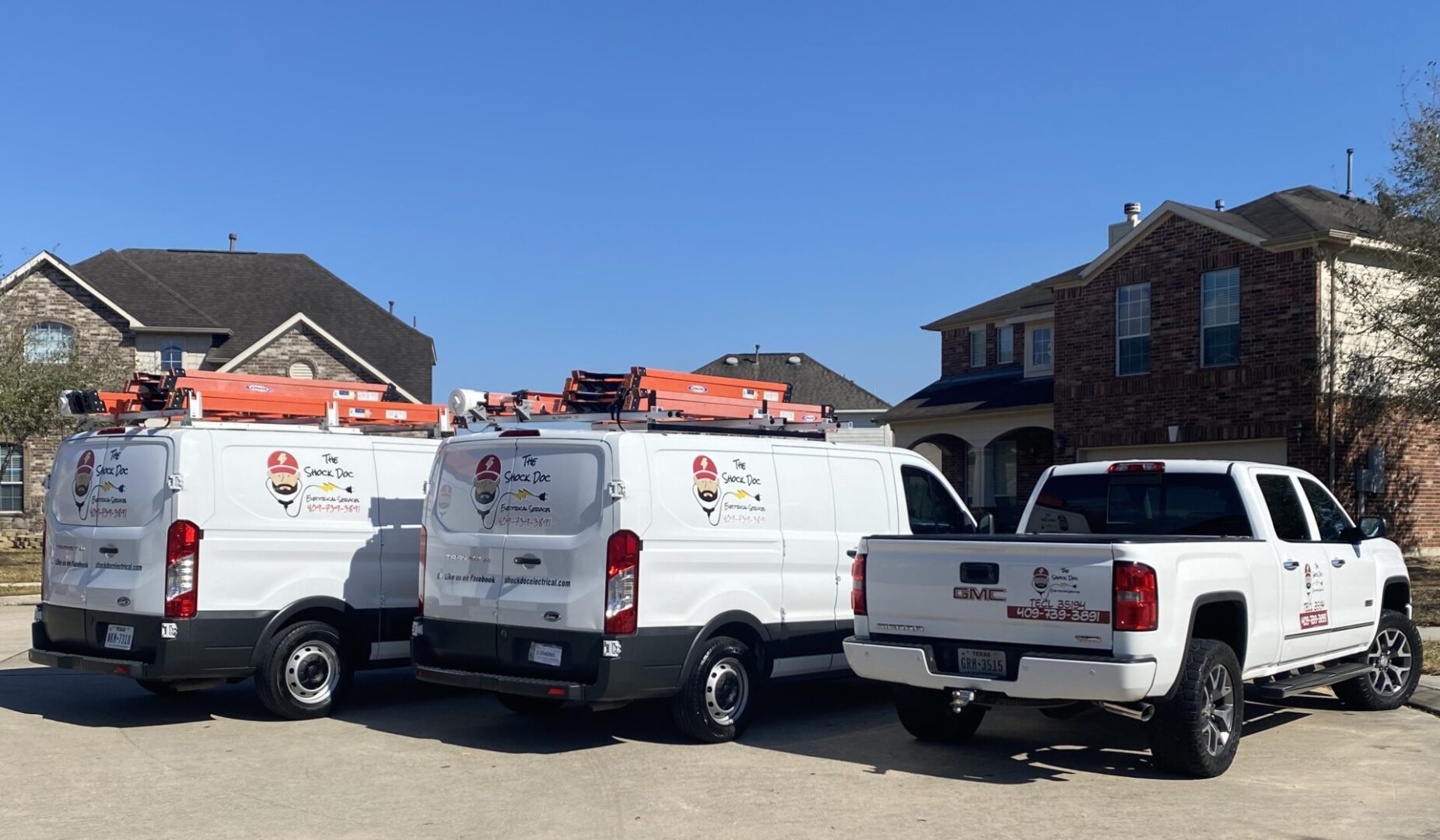 Two white utility vans parked on a residential street under a clear blue sky.