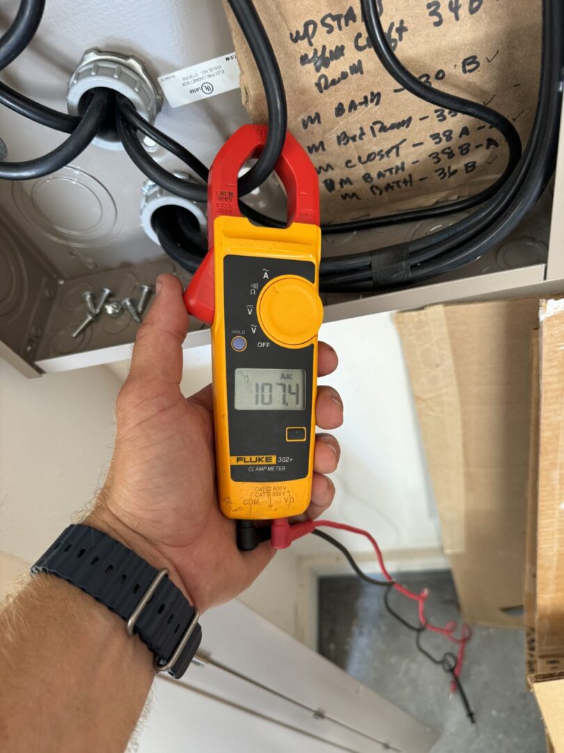 Hand holding a digital clamp meter with red and black probes.