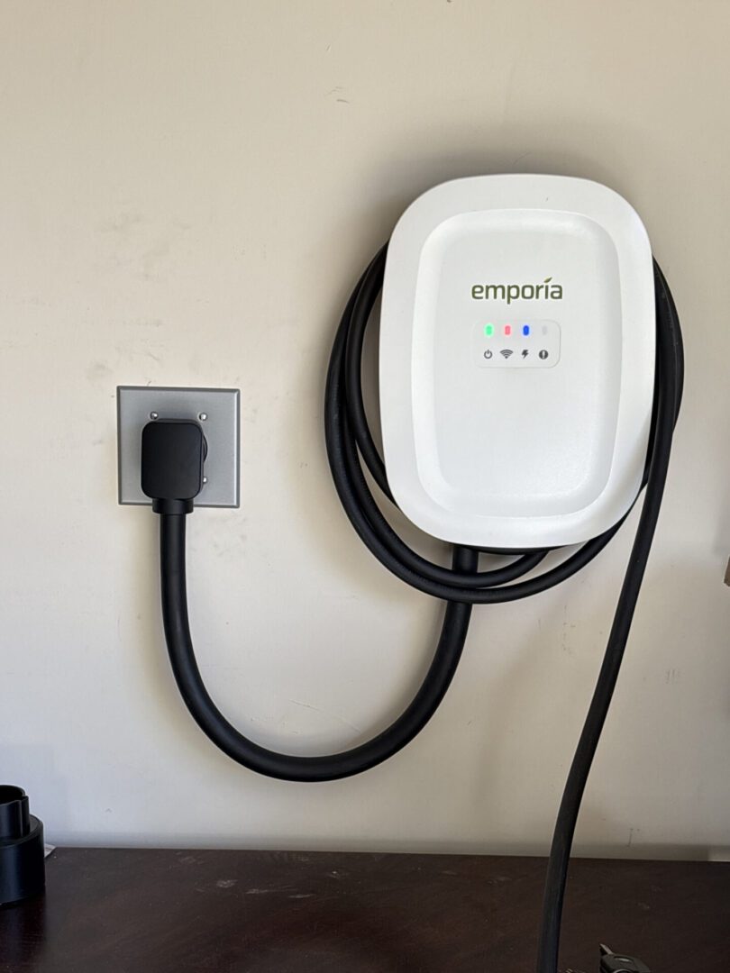 A white Emporia device plugged into a wall socket with a coiled black cable.