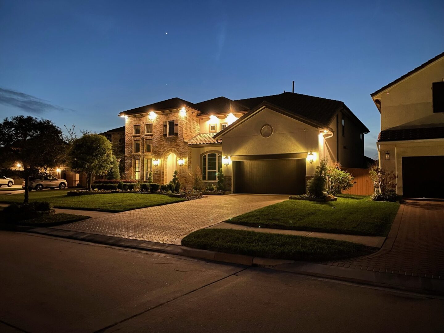 A well-lit suburban house at dusk with a driveway and garage.